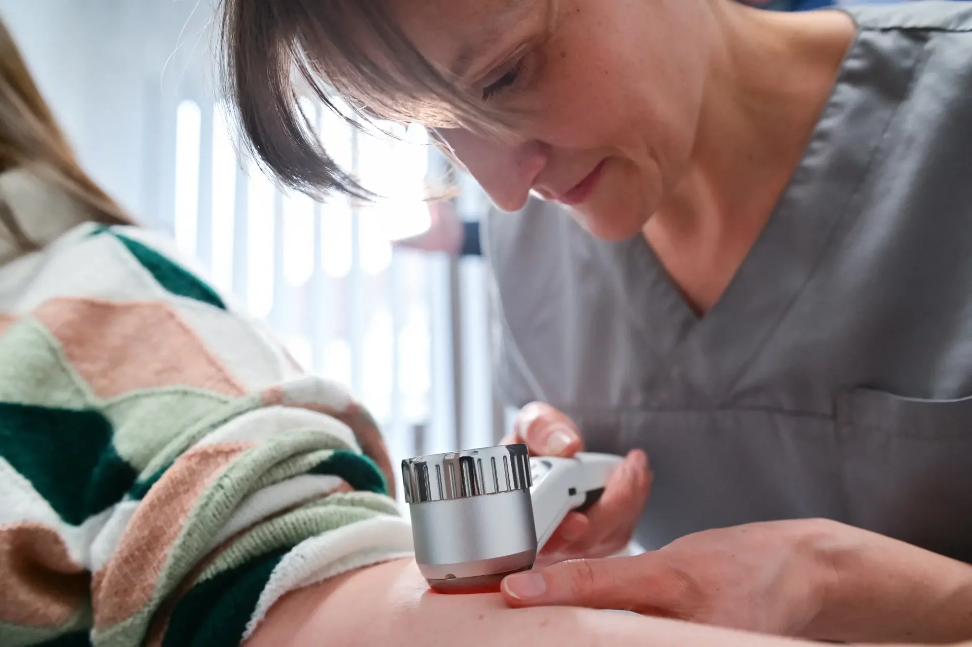 Dr. Ella Grosch untersucht den Arm einer Patientin mit einem Lupen Instrument
